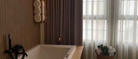 A modern bathroom with a freestanding bathtub, wooden paneling, a towel rack, and a window with sheer curtains.