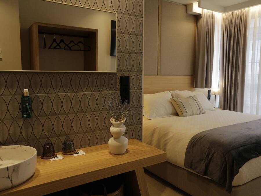 A hotel room with a bed, bedside table, and a mirror.