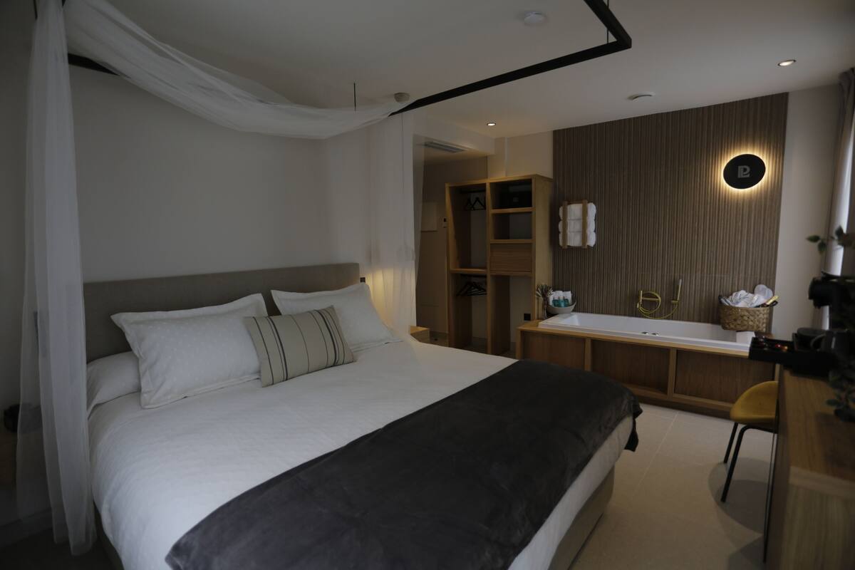 Ein Schlafzimmer mit einem großen Bett, einem Nachttisch, einem Sessel, einem Kleiderschrank und einem Badezimmer mit Waschbecken und Spiegel.