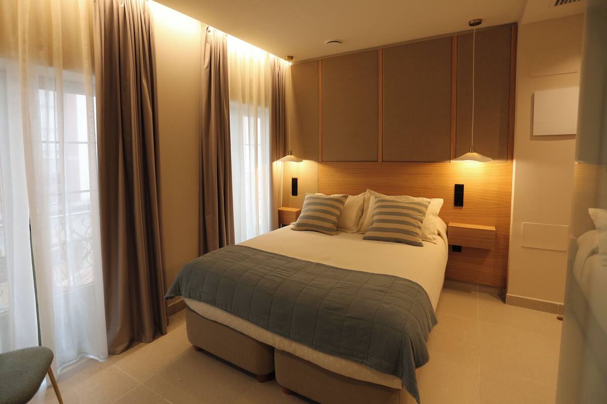 Ein Schlafzimmer mit Bett, Vorhängen, einem Nachttisch und einer Wandlampe.