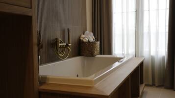 A bathroom with a wooden vanity, a bathtub, and a window with curtains.