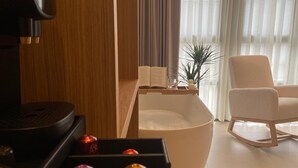 A modern living room with a coffee machine, a white sofa, a rocking chair, and a side table with a book and a glass. - Hotel Puerto de Luarca  (Valdes)