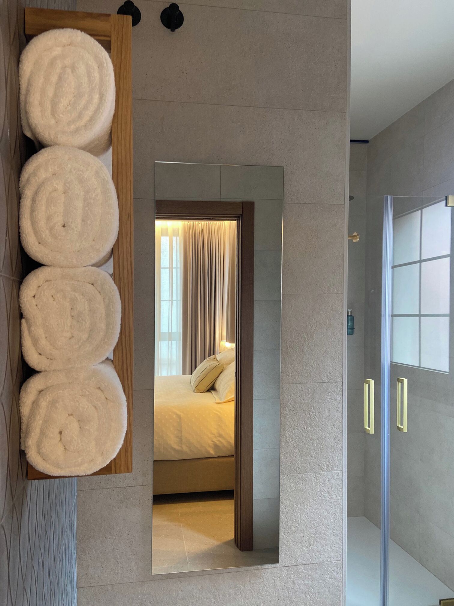 Une salle de bain moderne avec un grand miroir, un porte-serviettes en bois sur lequel sont pliés des serviettes, et une cabine de douche en verre.
