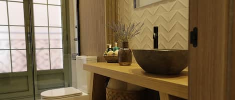 Un baño moderno con tocador de madera, un lavamanos grande tipo cuenco y un inodoro.