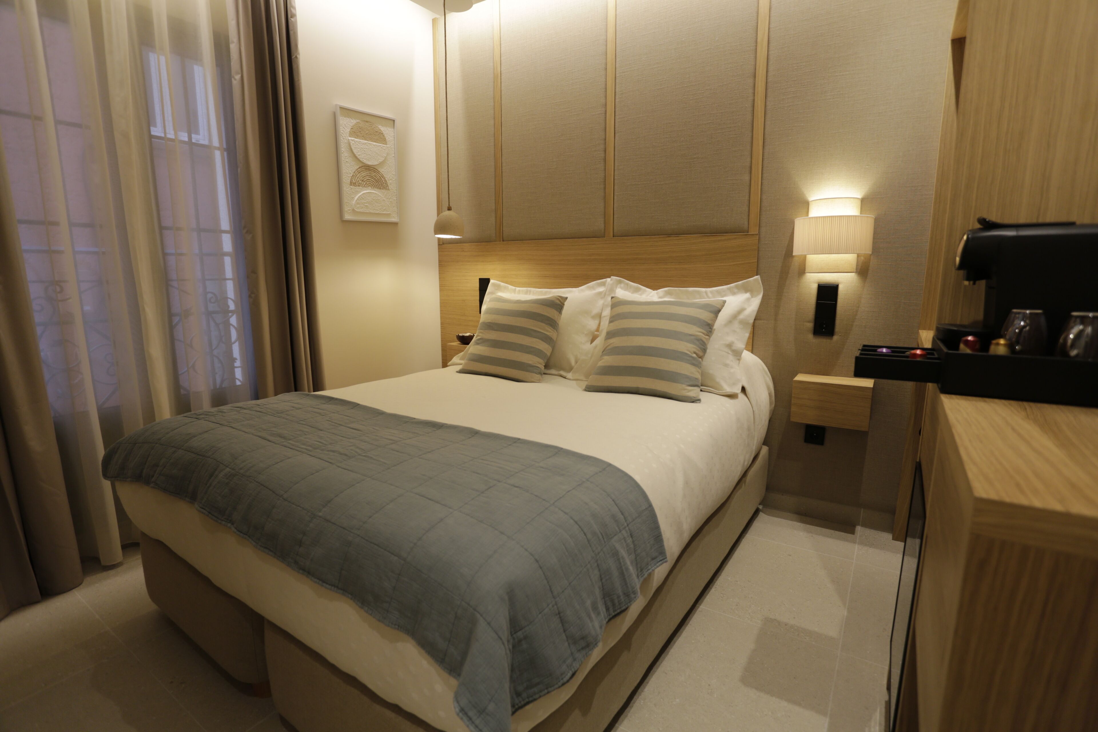 A hotel room with a bed, bedside tables, a lamp, and a coffee machine.