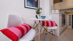 Une cuisine moderne avec des armoires blanches, une cuisinière et un plan de travail. On y trouve une petite table avec une plante et un bol. Deux chaises aux coussins rayés rouges et blancs sont placées devant la table.