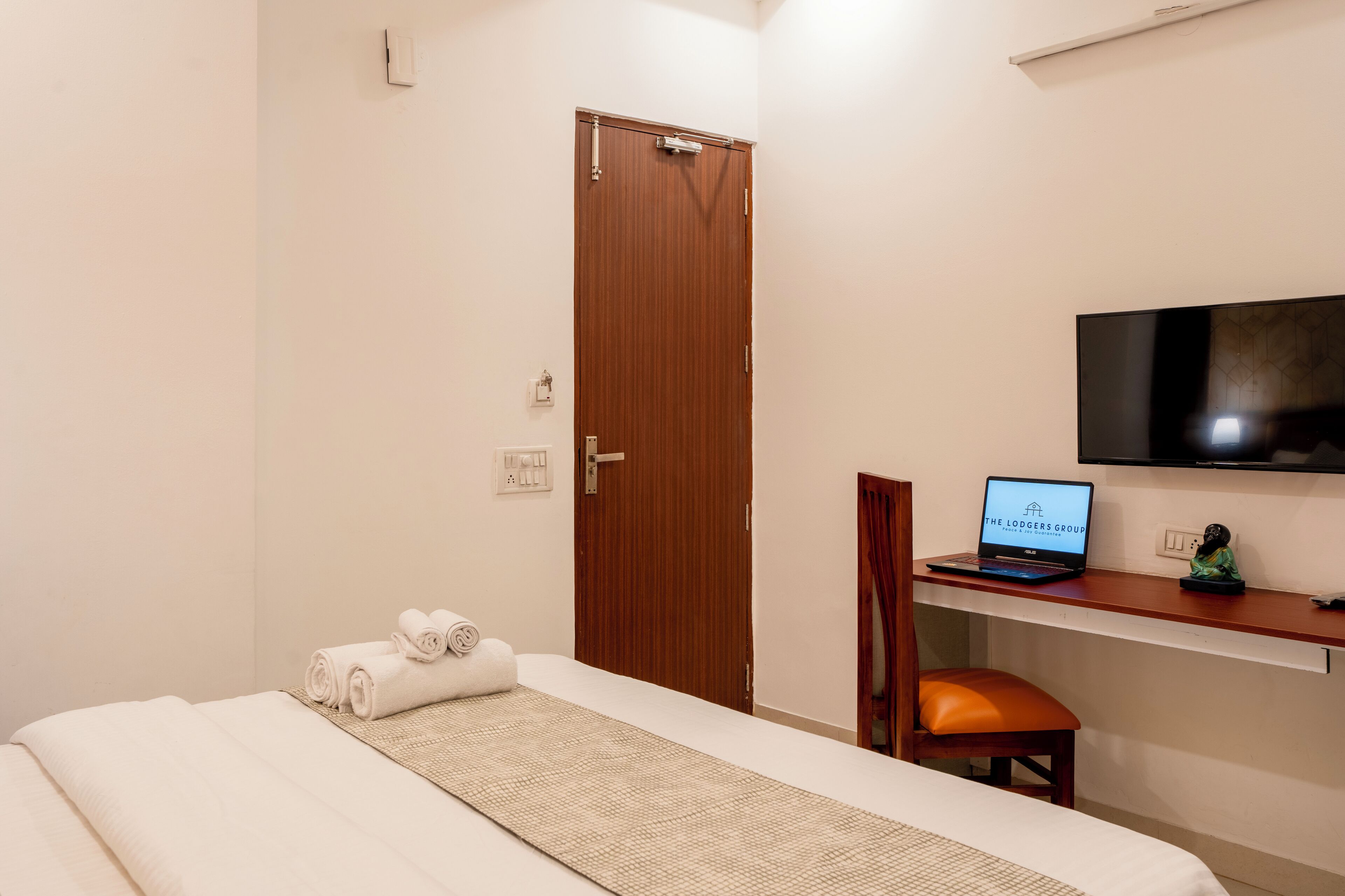 A hotel room with a bed, a desk with a laptop, a television, and a door.