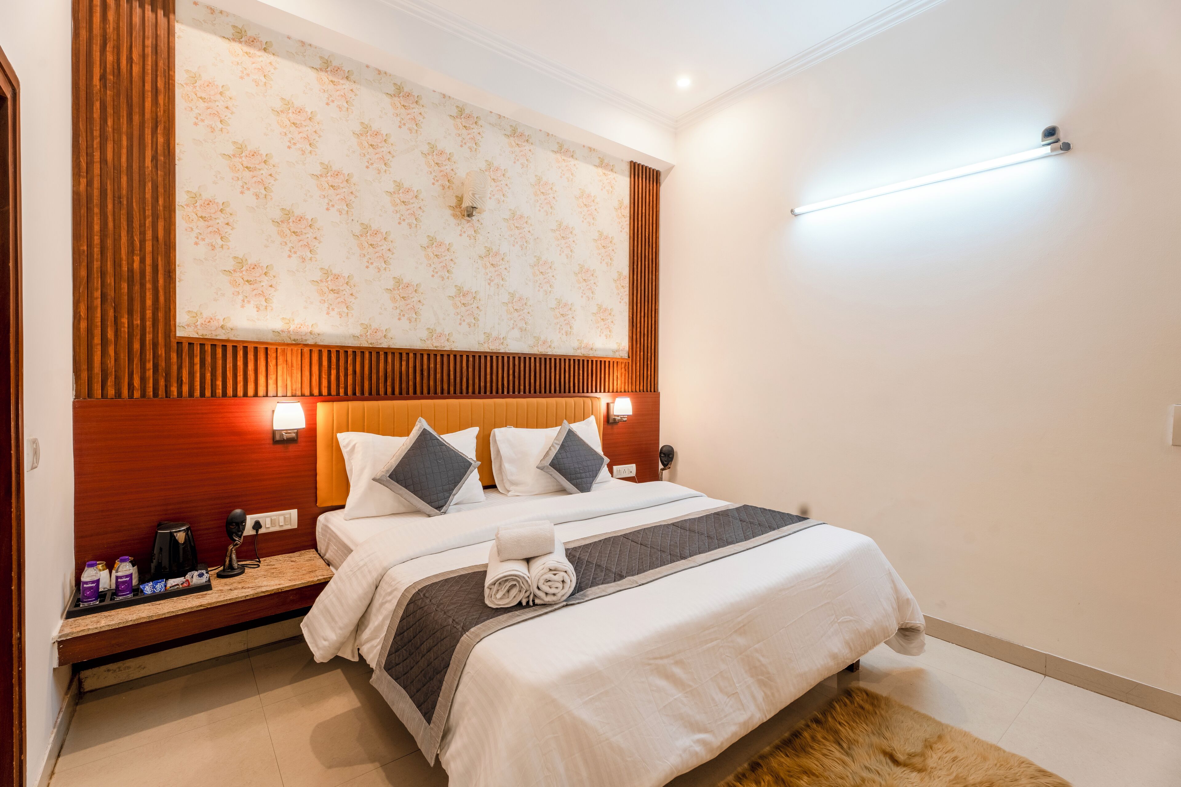 A hotel room with a bed, a nightstand, a wall-mounted light, and a ceiling light.