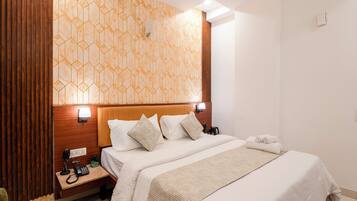 Ein Hotelzimmer mit einem hölzernen Kopfteil, einer Wand mit geometrischem Muster, einem Bett mit weißer Bettwäsche, einem Nachttisch mit Lampe, einem Telefon und einer kleinen Pflanze.