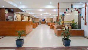 A hotel reception area with a wooden reception desk, seating area, potted plants, and a television screen. - The Lodgers Hotel and Banquet Sector 38 (Gurugram)