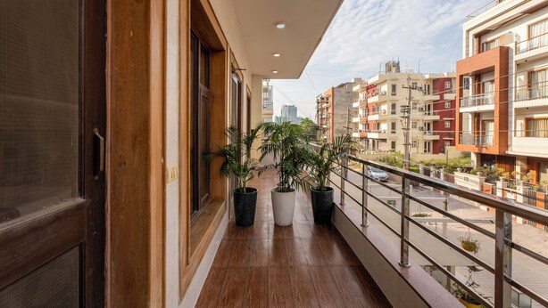 A balcony with wooden flooring, potted plants, and a view of surrounding buildings. - The Lodgers Hotel and Banquet Sector 38 (Gurugram)