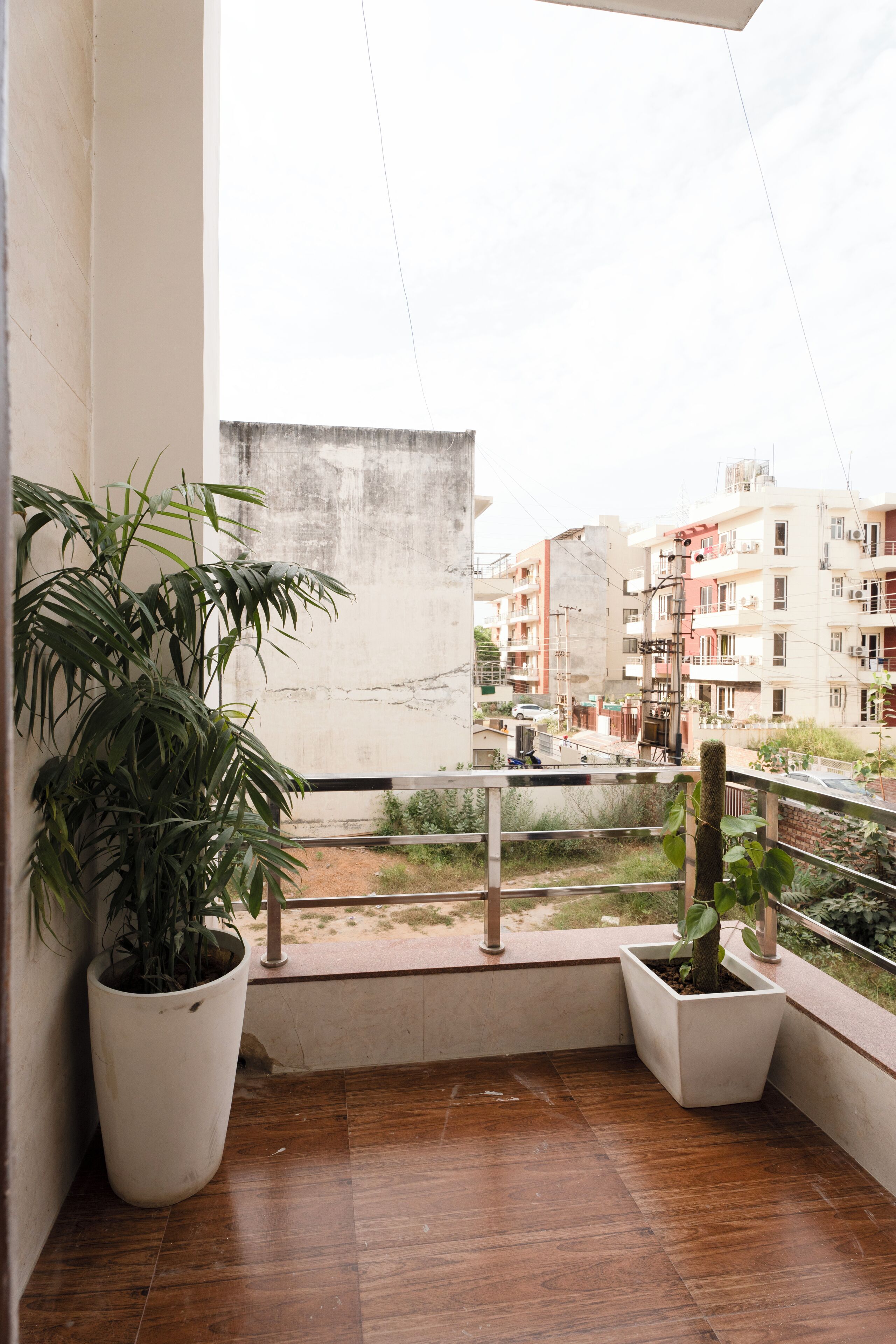 A balcony with two potted plants, a view of a cityscape, and a tiled floor.