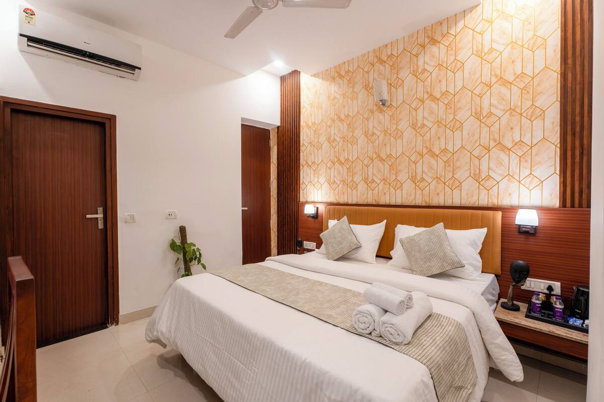 Habitació d'hotel amb un llit gran, un capçal de fusta, una làmpada penjada a la paret i una taula de nit amb coses de confort.