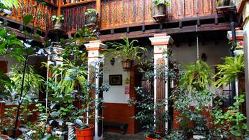 Un patio con plantas en macetas, columnas de madera y un balcón de madera con barandillas.