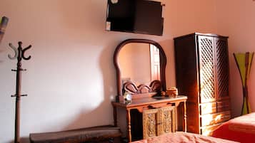 Une chambre à coucher avec un lit, une commode en bois, un miroir, un porte-manteau et un téléviseur fixé au mur.