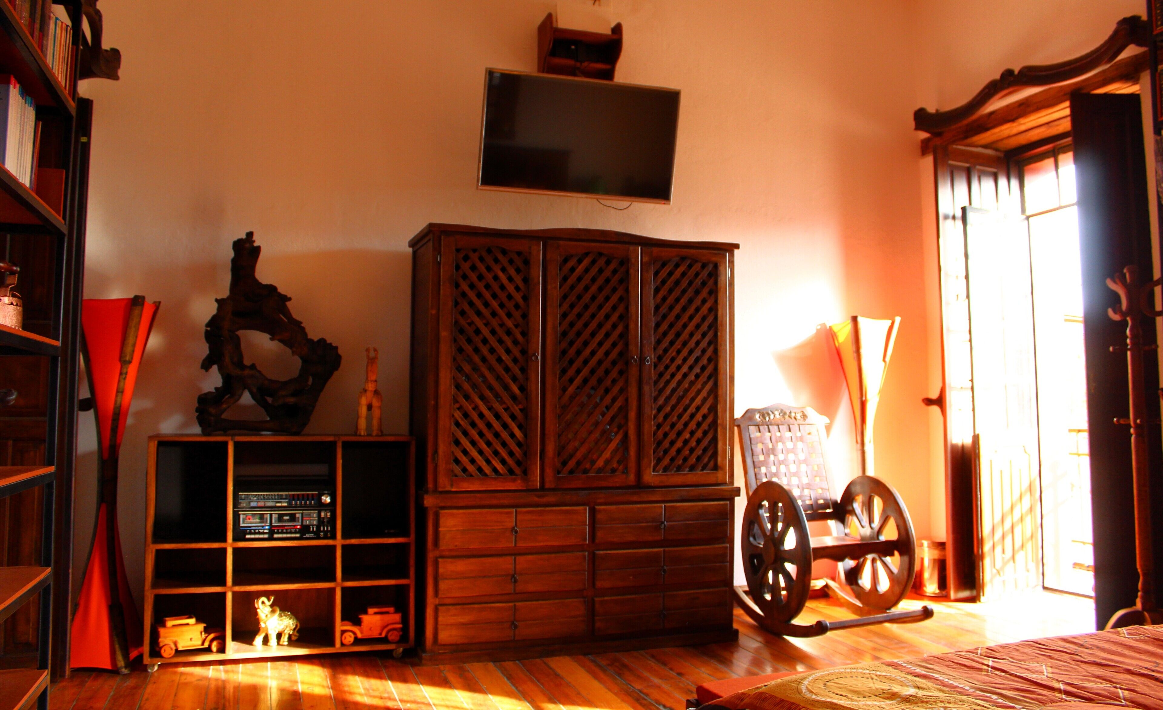 Une pièce avec un meuble en bois, un téléviseur fixé au mur, un fauteuil à bascule et une petite étagère remplie de jouets.