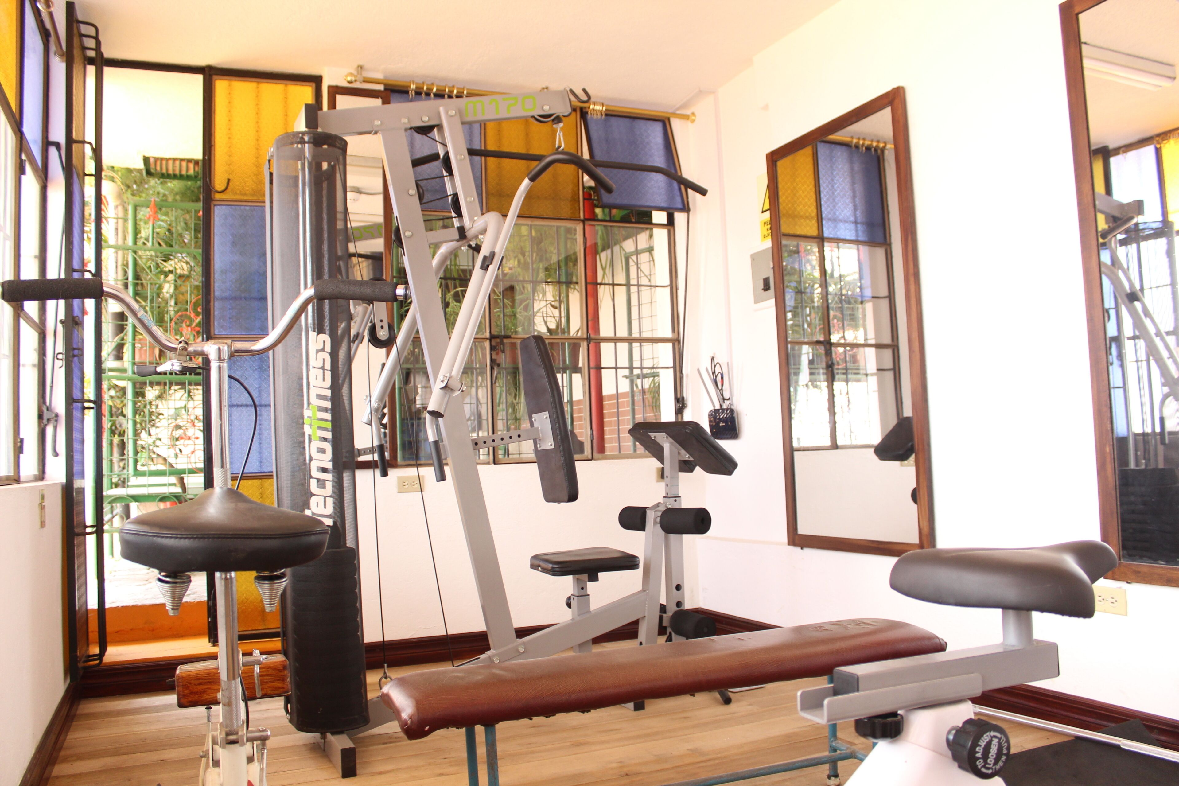 Een sportschool met trainingsapparatuur, grote ramen en een houten vloer.