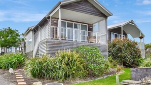 A two-story house with a balcony, surrounded by a garden with various plants and a small pond. - Ocean Mist at Caves Beach Villas (Caves Beach)