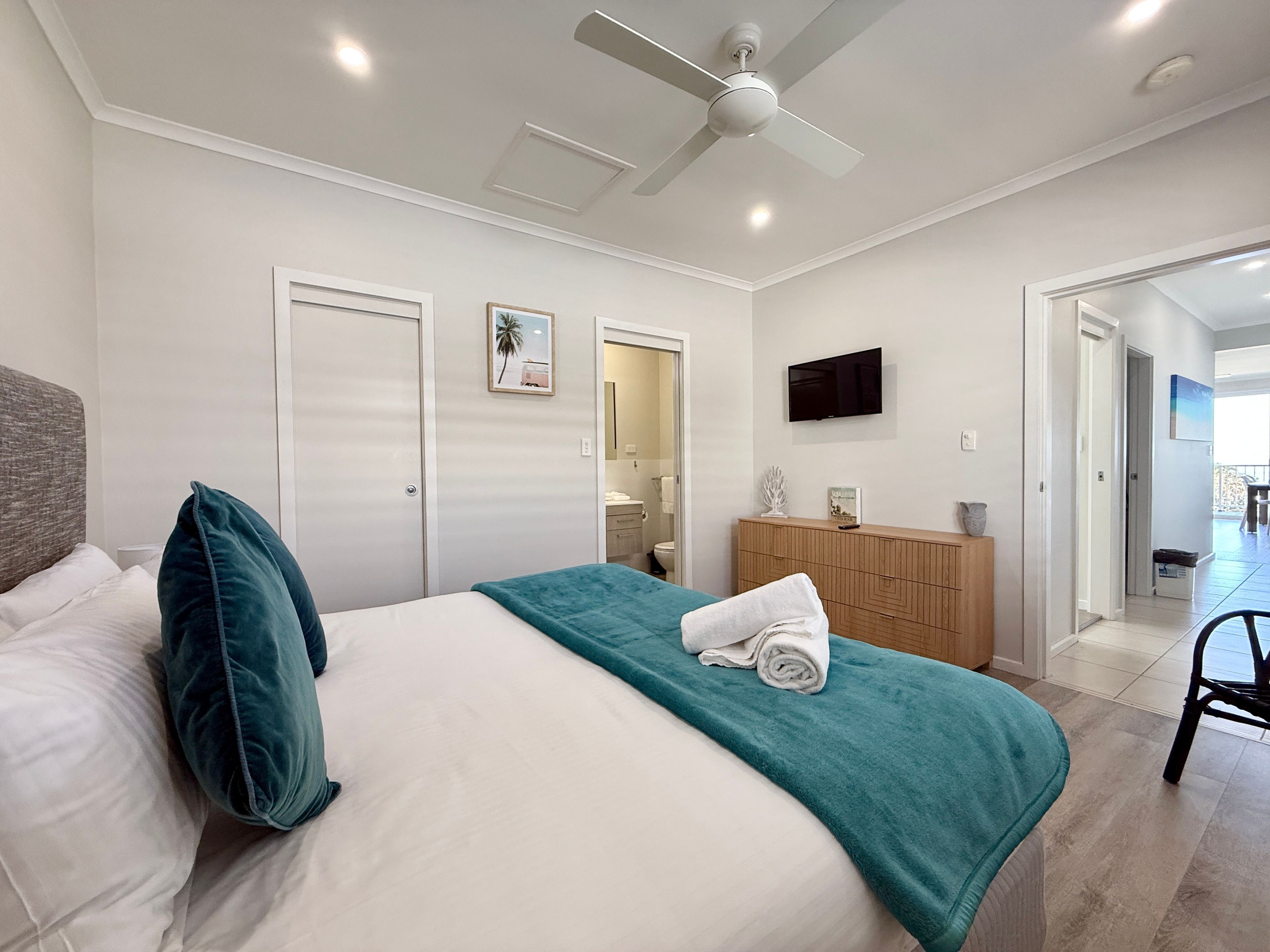 A hotel room with a bed, a ceiling fan, a TV, and a view of the outside.