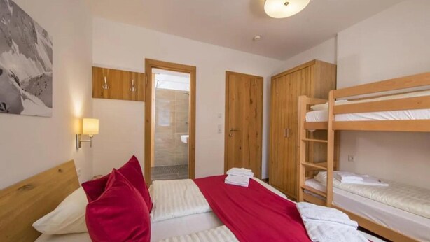Ein Hotelzimmer mit Etagenbett, einem Einzelbett, Holzschränken, einer Duschkabine und einer Wandlampe.