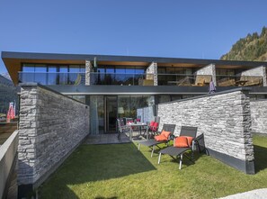 Situated in a mountainous area, this building offers a covered outdoor seating area with lounge chairs and a table.