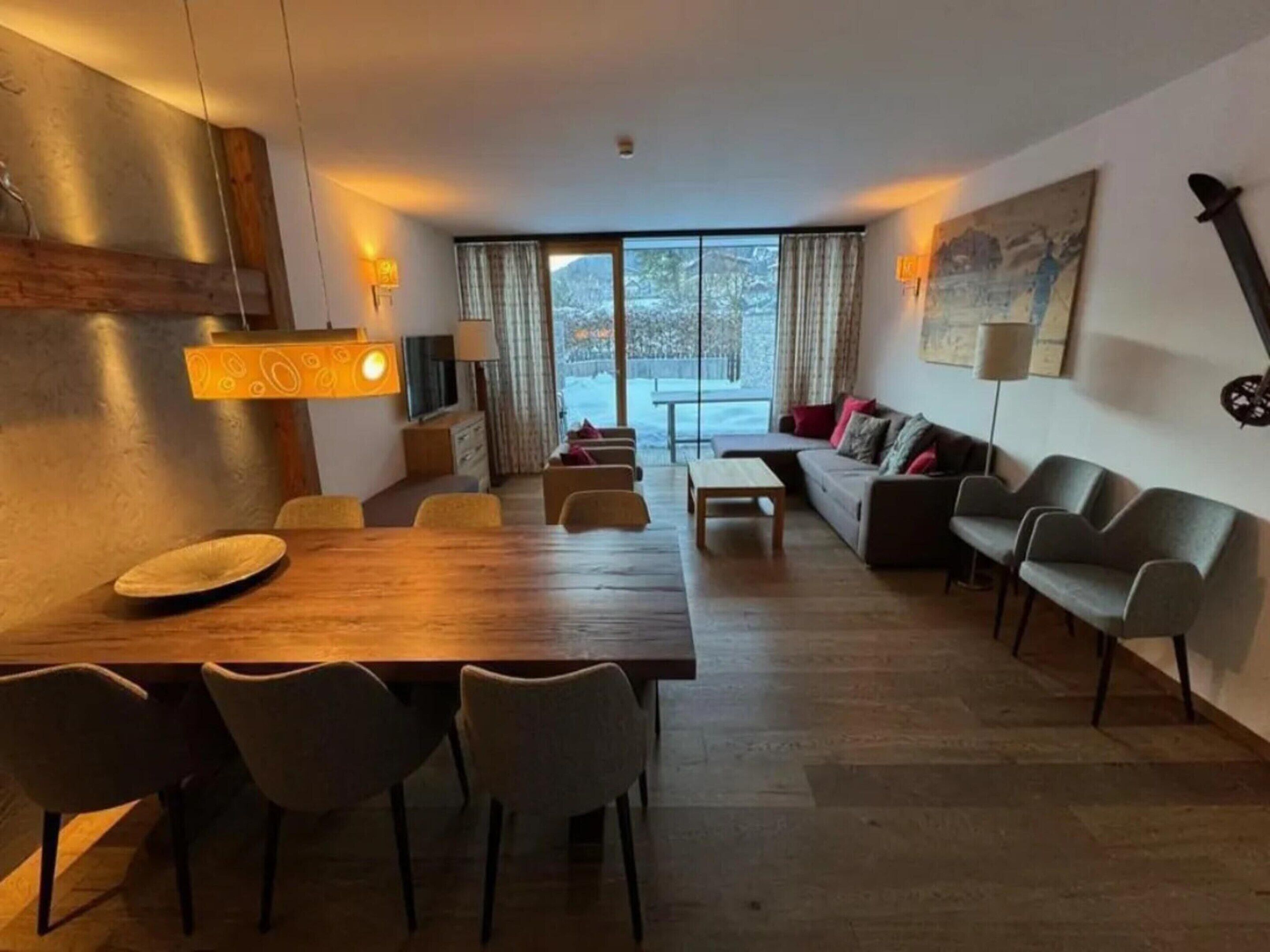 A modern living room with a wooden dining table, sofas, and a large window with a view.
