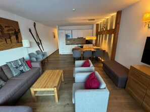 Ein modernes Wohnzimmer mit einer Couch, Sesseln, einem Couchtisch und einem Essbereich mit Stühlen und einem Tisch.