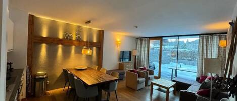 Una sala de estar moderna con una mesa de comedor de madera, asientos y un ventanal que ofrece vistas de un paisaje nevado.