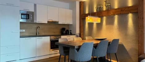 A modern kitchen with white cabinets, a microwave, and a dining area with a wooden table and four chairs.