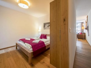 A bedroom with a wooden bed, a wooden wardrobe, and a view into a living area. - Elegant Neukirchen Apartment for 8 (Neukirchen am Grossvenediger)