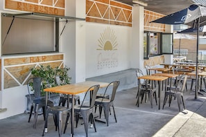 Un área de estar al aire libre con mesas y sillas, un letrero que dice 'Ocean Soul Espresso' y un panel de menú con el título 'Wild'.