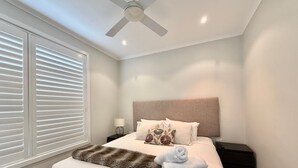 A bedroom with a bed, a nightstand, a lamp, a ceiling fan, and a window with blinds.