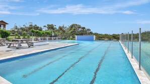 A swimming pool with clear blue water, surrounded by a fence, and picnic tables on the left.