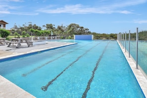 Una piscina con agua cristalina azul, rodeada por una valla, y mesas de picnic a la izquierda.