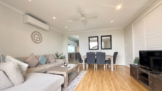 A living room with a sofa, coffee table, dining table with chairs, a TV, and a ceiling fan.