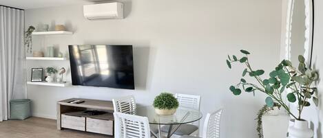 A modern living room with a flat-screen TV, white furniture, and a potted plant.