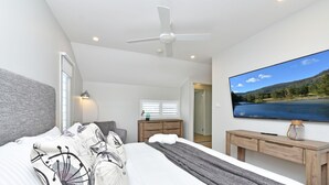 Una camera da letto moderna con un letto, una scrivania, una televisione e una ventola a soffitto.