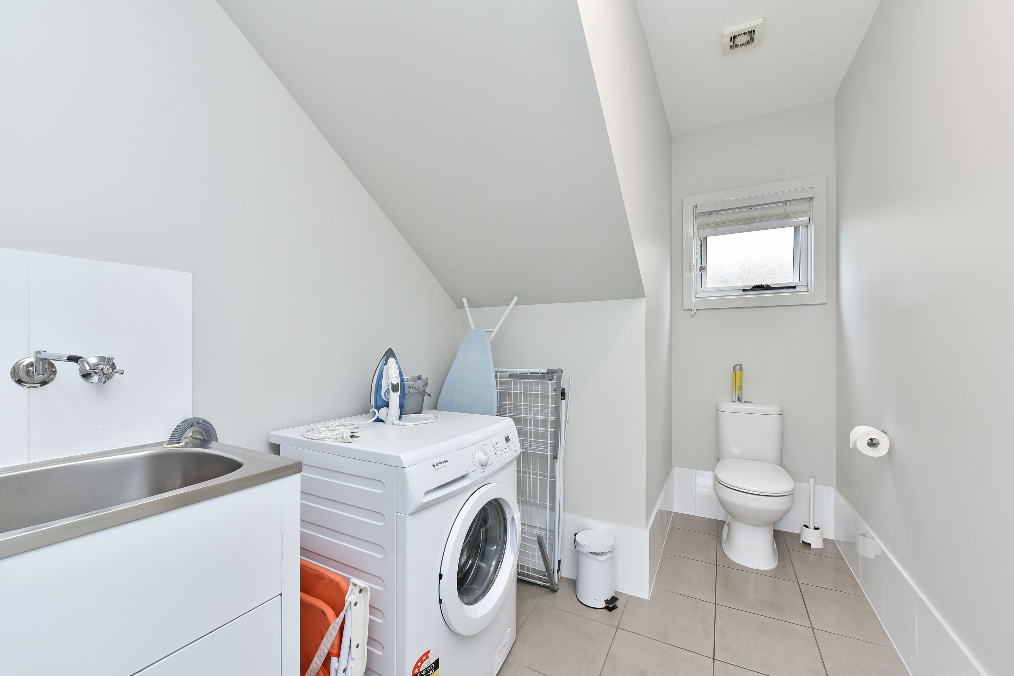 A compact, modern bathroom with a built-in washing machine, a toilet, and a shower area.