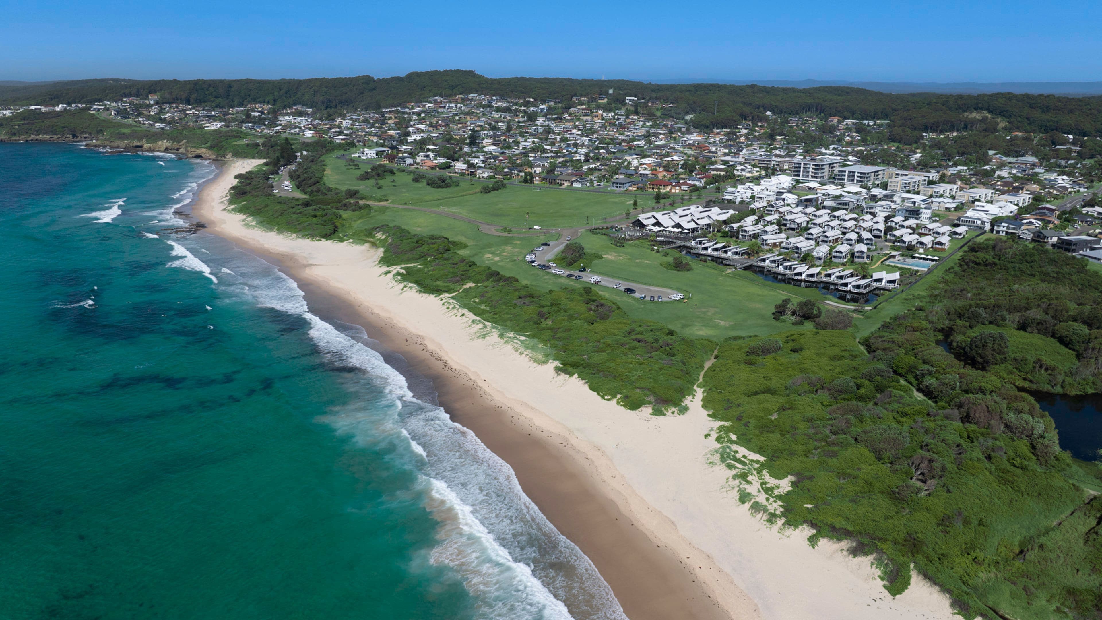 An aerial view of a coastal town with a beach, residential areas, and a golf course.