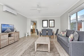 Un salon moderne avec un canapé gris, une table basse en bois et un téléviseur posé sur un meuble en bois.