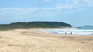 A beach with a sandy shore, a grassy hill in the background, and a clear sky. - Beach Escape at Caves Beach Villas (Caves Beach)