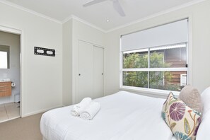 Una habitación de hotel con cama, ventana con vista a follaje, baño con inodoro y lavamanos, y un ventilador de techo.