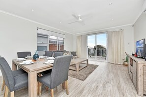 A modern dining area with a wooden table set for four, grey upholstered chairs, and a large window with blinds.