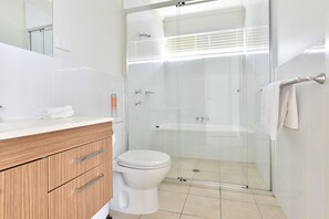 Un baño moderno con ducha envuelta en vidrio, inodoro blanco y tocador de madera con espejo.