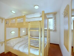 A bunk bed room with a wooden ladder, a window with curtains, and a wall-mounted hook.