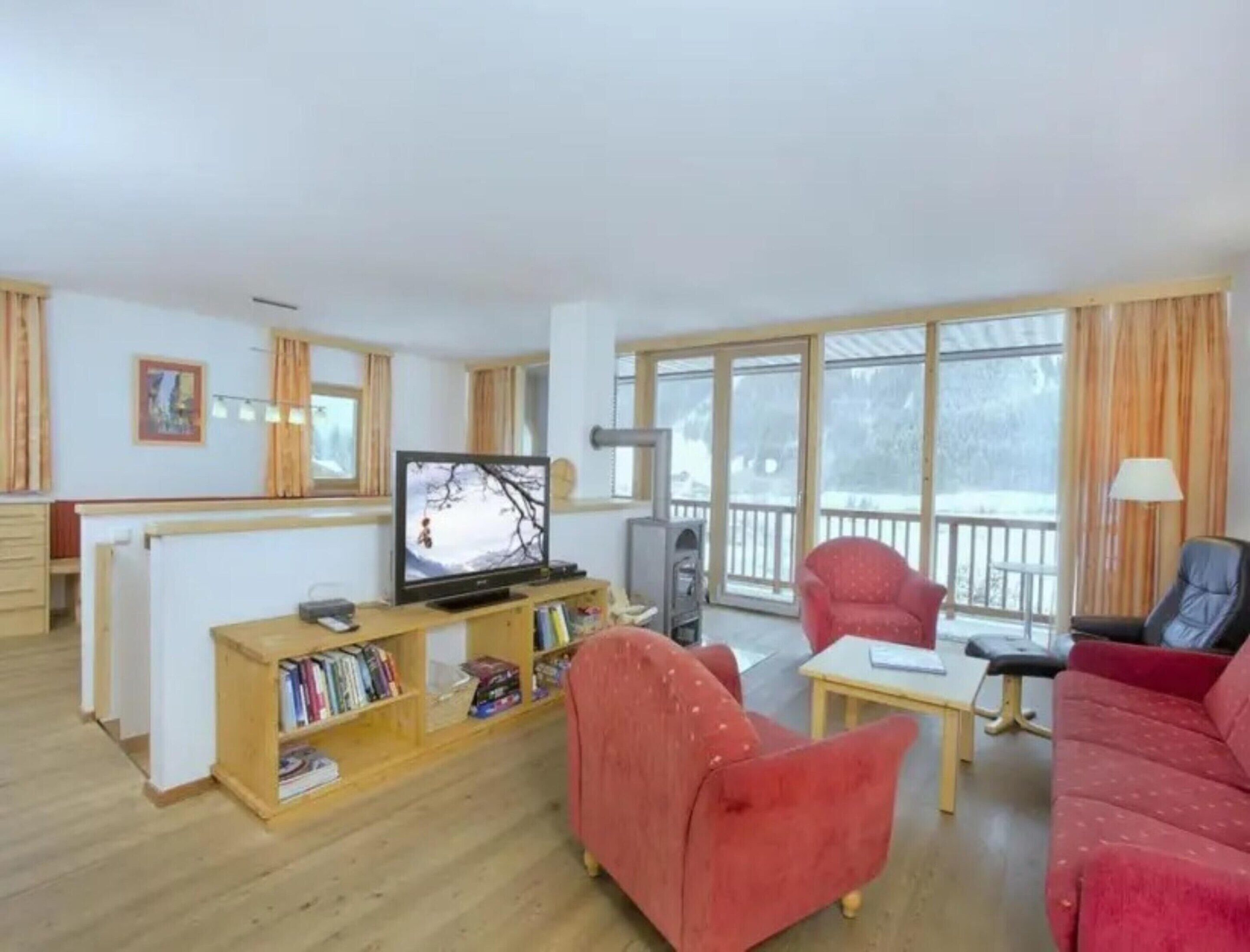 A living room with a television, a red sofa, a bookshelf, and a balcony with a view.