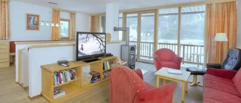A living room with a television, a red sofa, a bookshelf, and a balcony with a view.