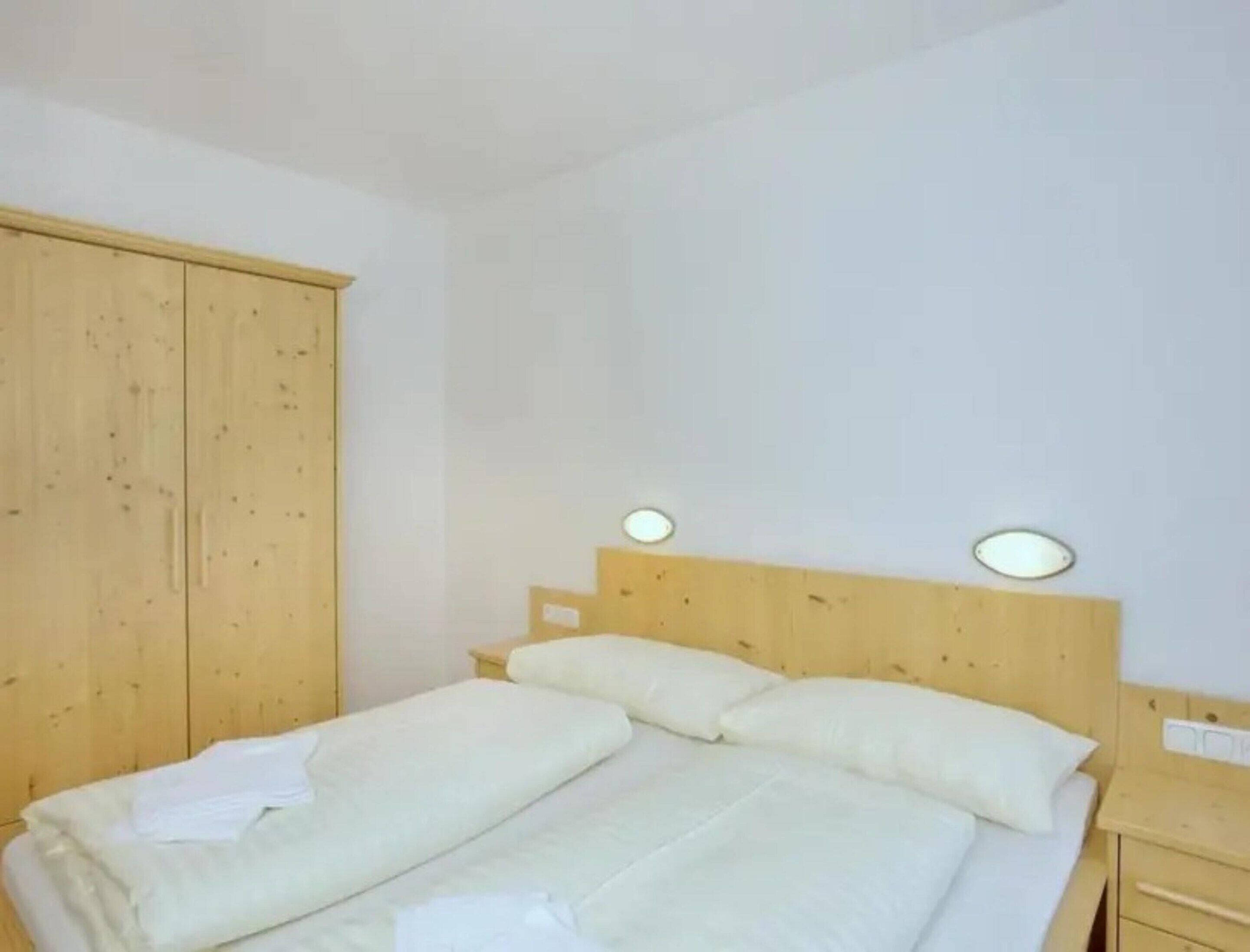Un lit simple avec une literie blanche, dans une pièce aux murs et à l’armoire en bois.