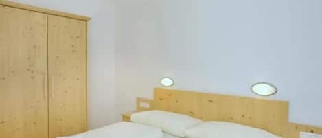 Un lit simple avec une literie blanche, dans une pièce aux murs et à l’armoire en bois.