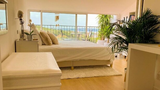 Un dormitorio con una cama grande, una mesita de noche, un aparador y un balcón con vistas al paisaje.